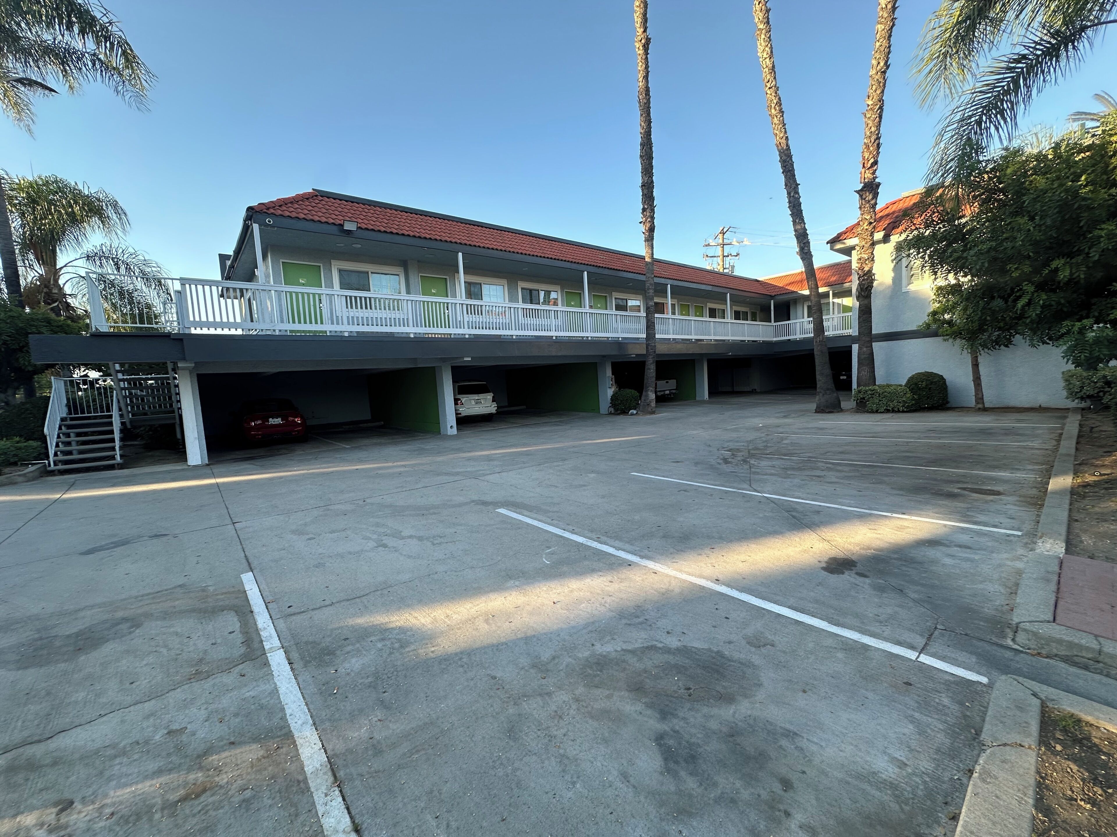 A multi-story parking garage with a covered walkway, palm trees, and a building with a red-tiled roof.