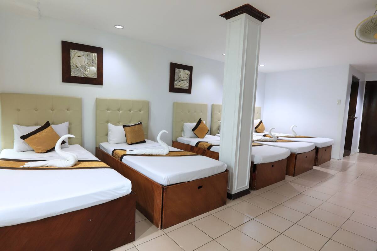 A hotel room with four beds, each with a headboard, white bedding, and decorative swan pillows.