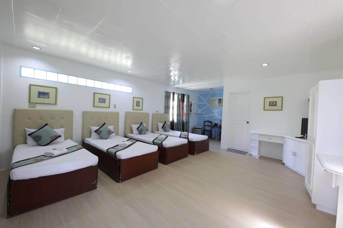 A hotel room with four beds, a desk, and a TV.