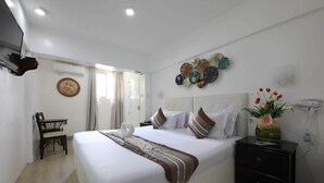 Ein ordentlich eingerichtetes Hotelzimmer mit einem großen Bett, Nachttischen, einem kleinen Schreibtisch und einem an der Wand befestigten Fernseher.