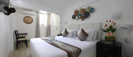 Ein ordentlich eingerichtetes Hotelzimmer mit einem großen Bett, Nachttischen, einem kleinen Schreibtisch und einem an der Wand befestigten Fernseher.