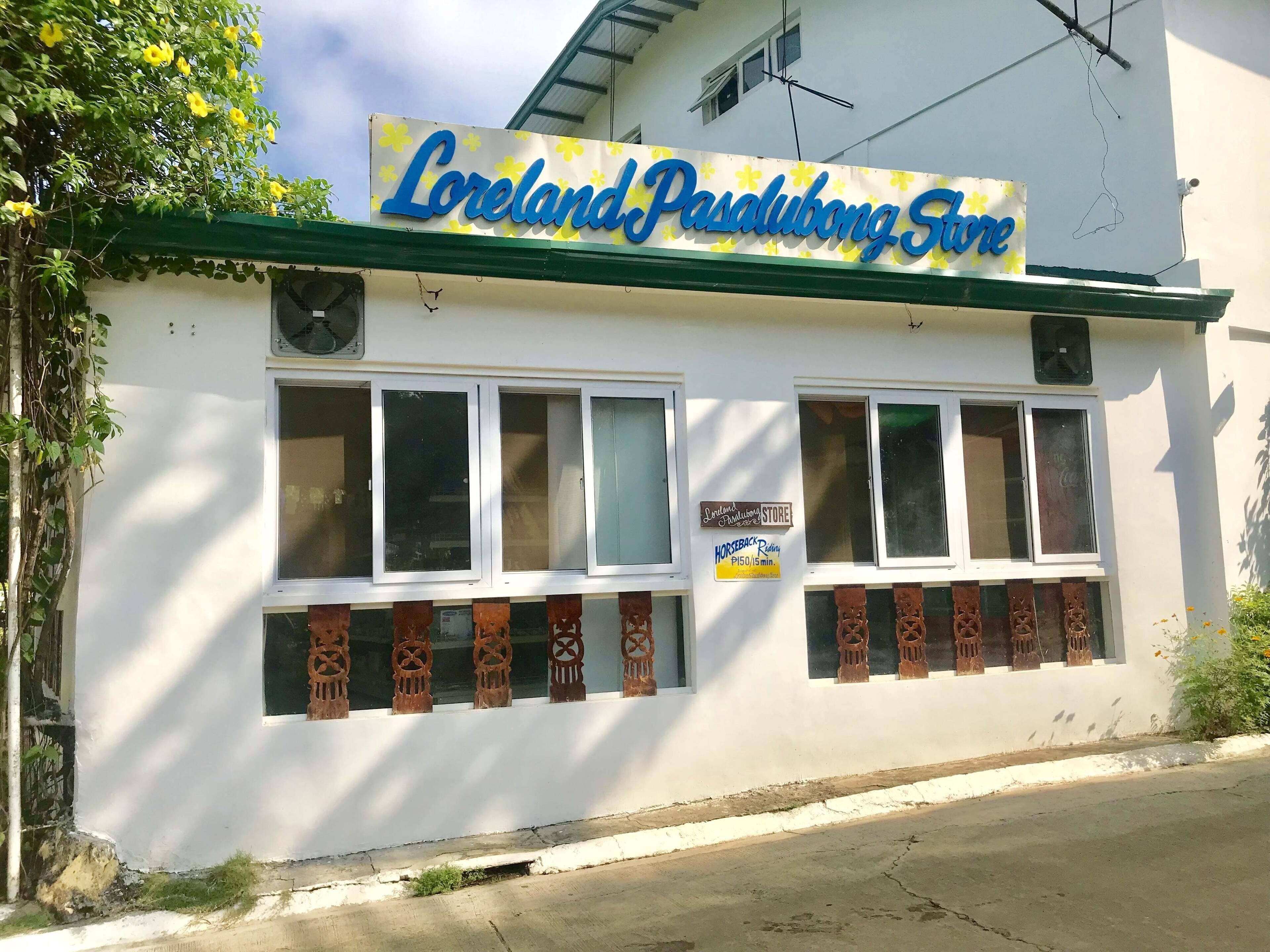 Una fachada con un letrero que dice "Lorland Pasalubong Store" y un anuncio debajo que ofrece un paseo a caballo por 150 pesos.