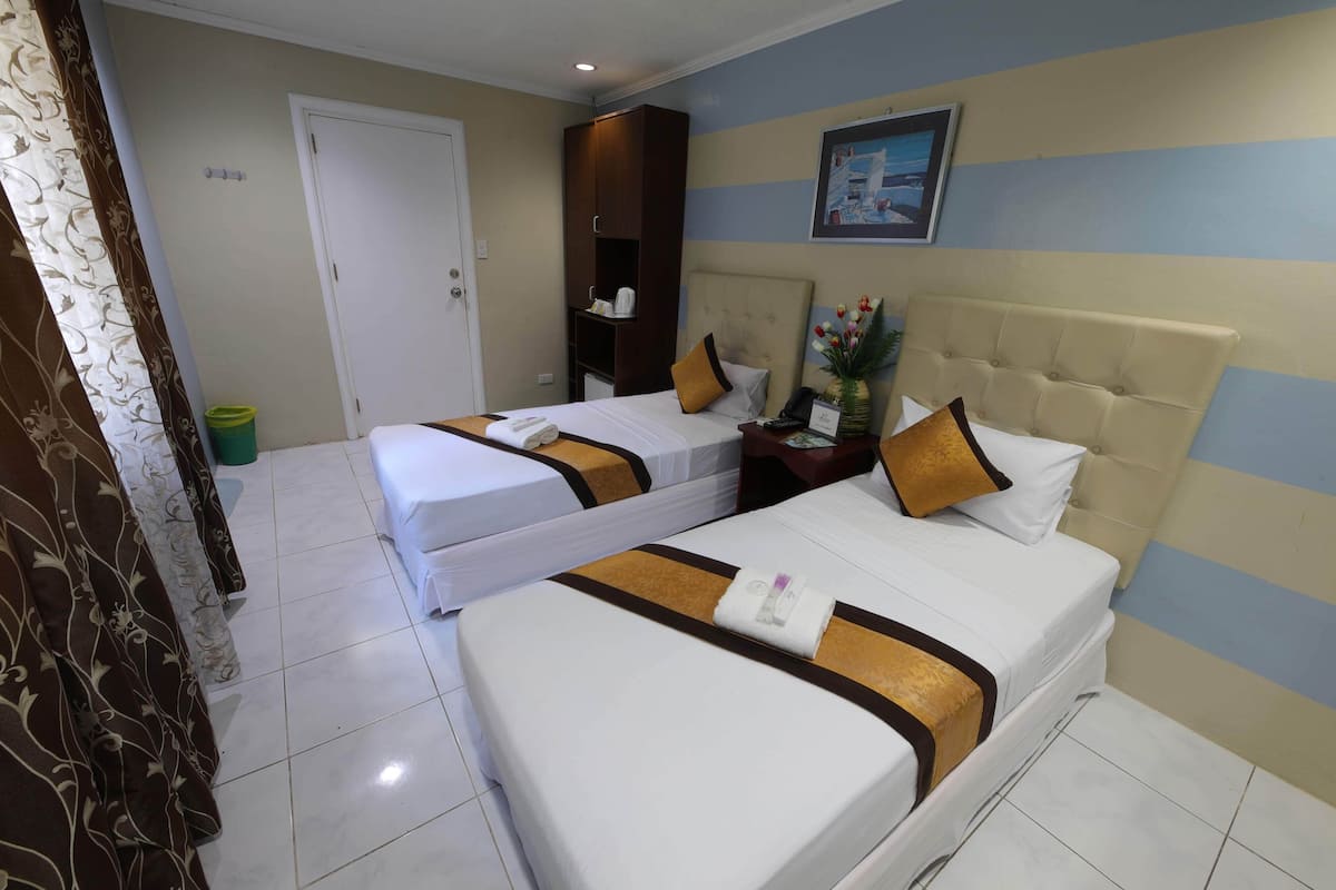 A hotel room with two beds, a wardrobe, a nightstand, and a painting on the wall.