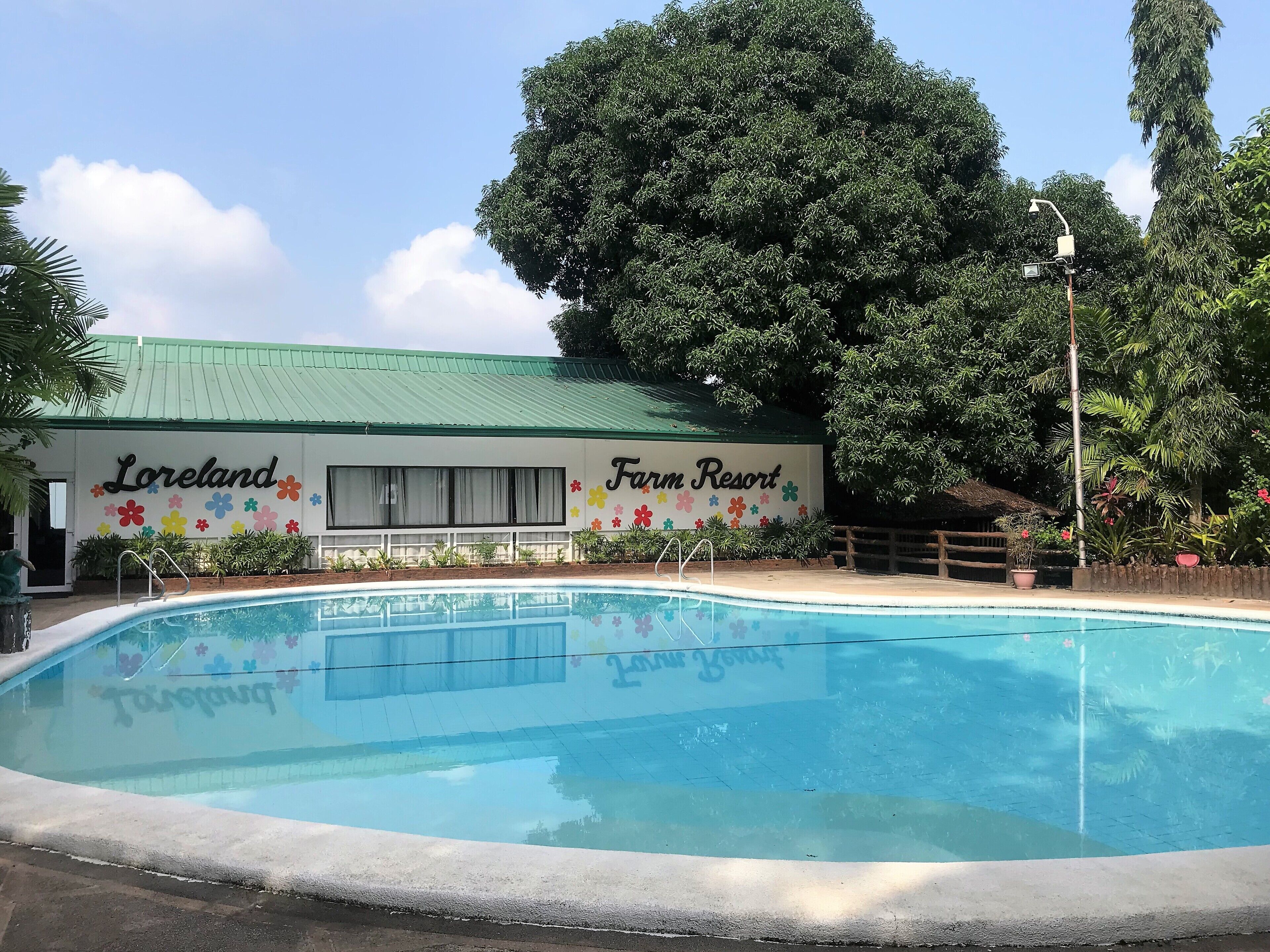 A pool area with a sign reading "Loreland Farm Resort" and a building with a green roof.