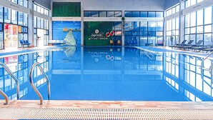 An indoor swimming pool with clear blue water, surrounded by windows and a colorful ceiling.
