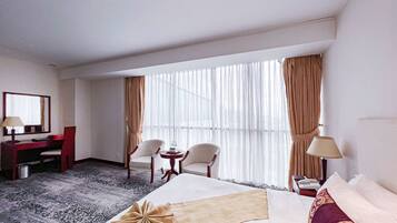 A hotel room with a large bed, two chairs, a desk, and a small table.