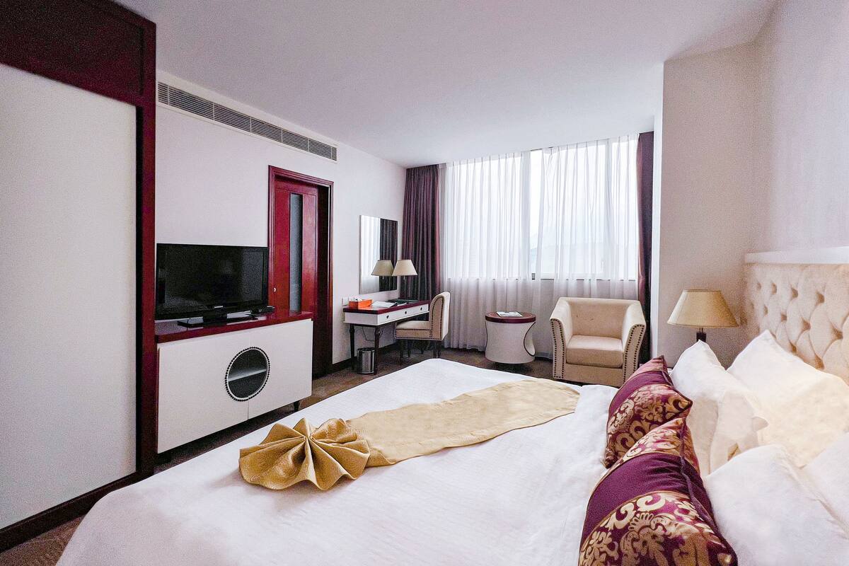 Hotellihuone, jossa on sänky, televisio, työpöytä, tuoli ja ikkuna, jossa on verhot.