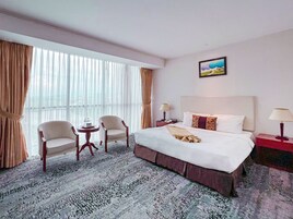 Habitación de hotel con una cama grande, dos sillones, una mesita y una mesita de noche con lámparas.