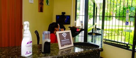 A reception desk with a sign indicating Wi-Fi availability, a bottle of hand sanitizer, and a water dispenser.