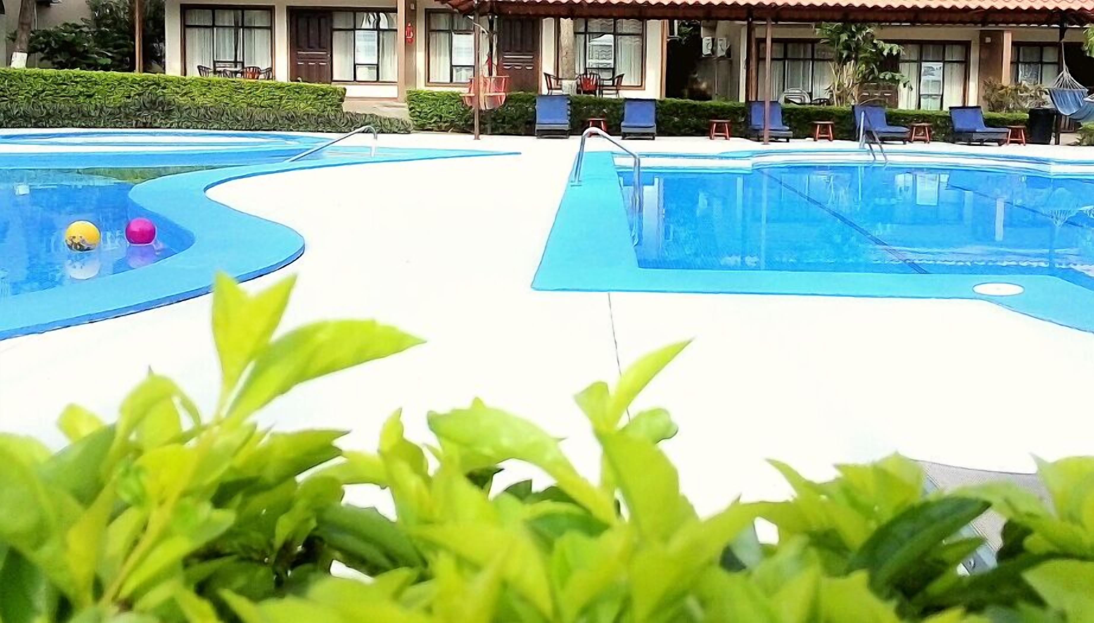 Zona de piscina con sillones de descanso y un edificio al fondo.