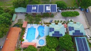 A building with multiple solar panels on the roof, a swimming pool, and a parking area. - Hotel & Villas Huetares (Sardinal)