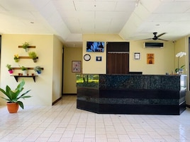 A reception area with a marble counter, potted plants, a television, and a clock on the wall.