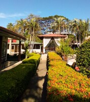 A pathway leading to a building with a red roof, surrounded by well-maintained gardens and palm trees.