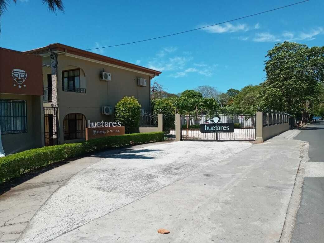 Entrada de hotel con un camino de acceso porticado, un letrero que dice 'Huites & Villas', y cielo despejado.