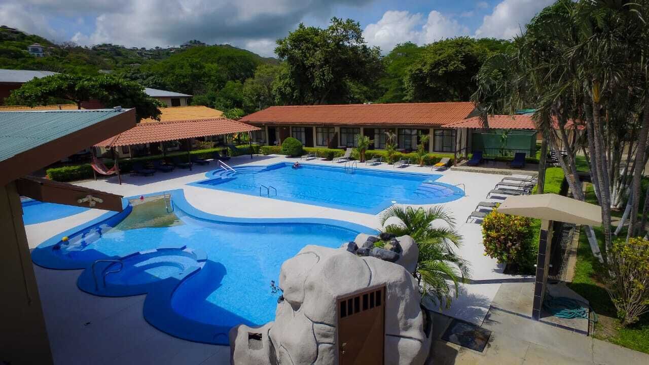 Ein Resort mit großem Pool, Liegestühlen und einem überdachten Bereich mit rotem Dach.