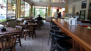 A restaurant with wooden tables and chairs, large windows, and a counter with a menu. - Hotel & Villas Huetares (Sardinal)