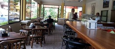 A restaurant with wooden tables and chairs, large windows, and a counter with a menu.