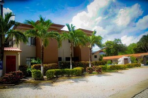 A building with a beige facade, palm trees, and a gravel driveway.