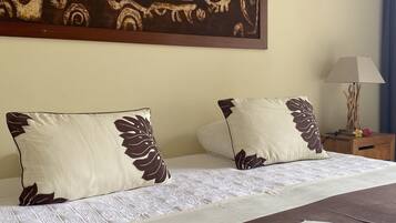 Una habitación de hotel con un cuadro decorativo grande, dos almohadas con motivos de hojas, una cama con cubrecama estampado con hojas y una mesita de noche con lámpara.