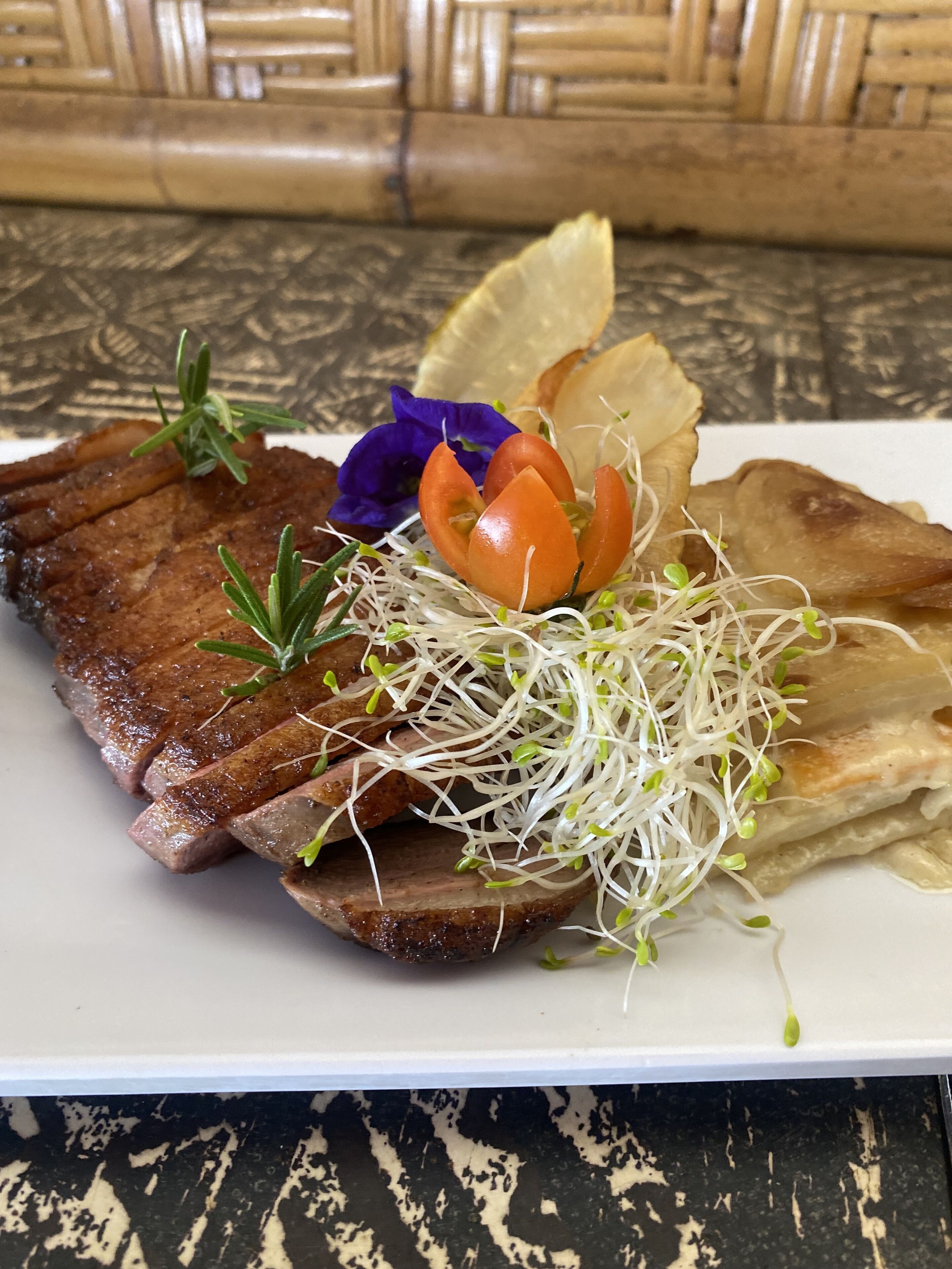 Un plato de comida con bistec, brotes, tomate y una flor.