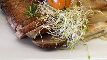 A plate of food with steak, sprouts, a tomato, and a flower.