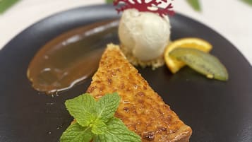 Ein Dessertteller mit Kuchenstück, einer Kugel Eis, einem Minzblatt und einem dekorativen rotem Korallenstück.