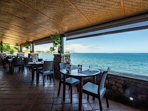 Dine al fresco with ocean views from this outdoor dining area, featuring tables and chairs amidst lush greenery.