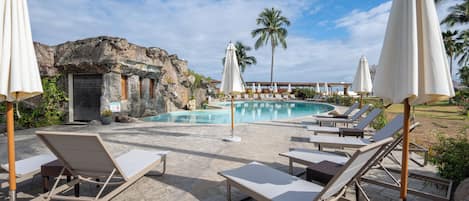A pool area with lounge chairs and umbrellas, a rocky backdrop, and a clear sky.
