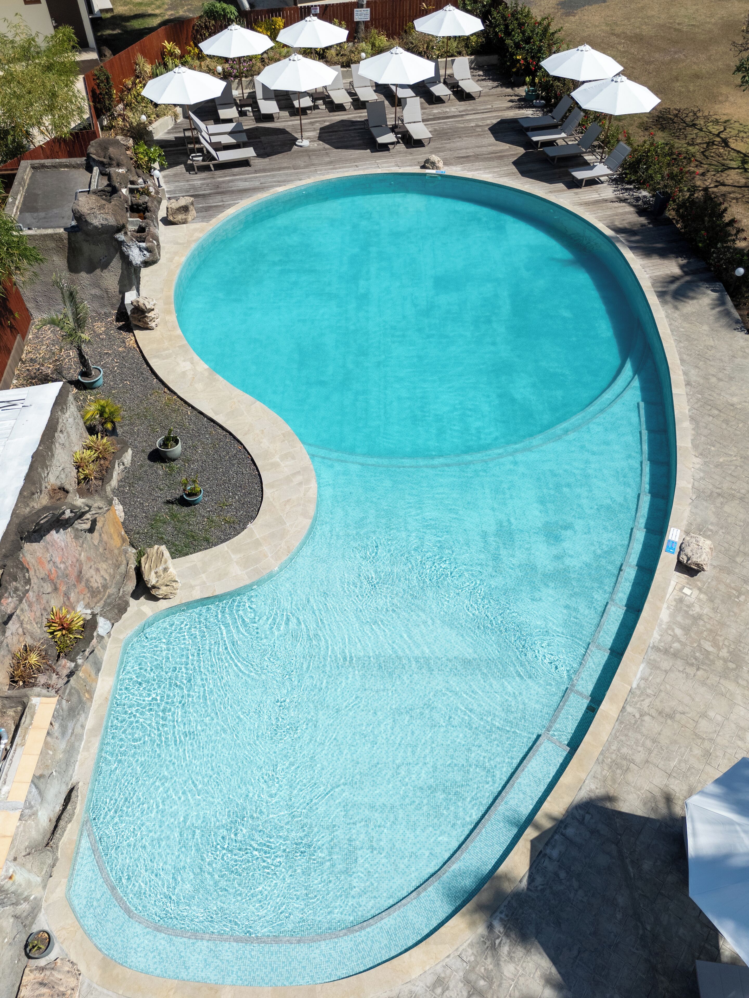A large, curved swimming pool with a wooden deck and lounge chairs.