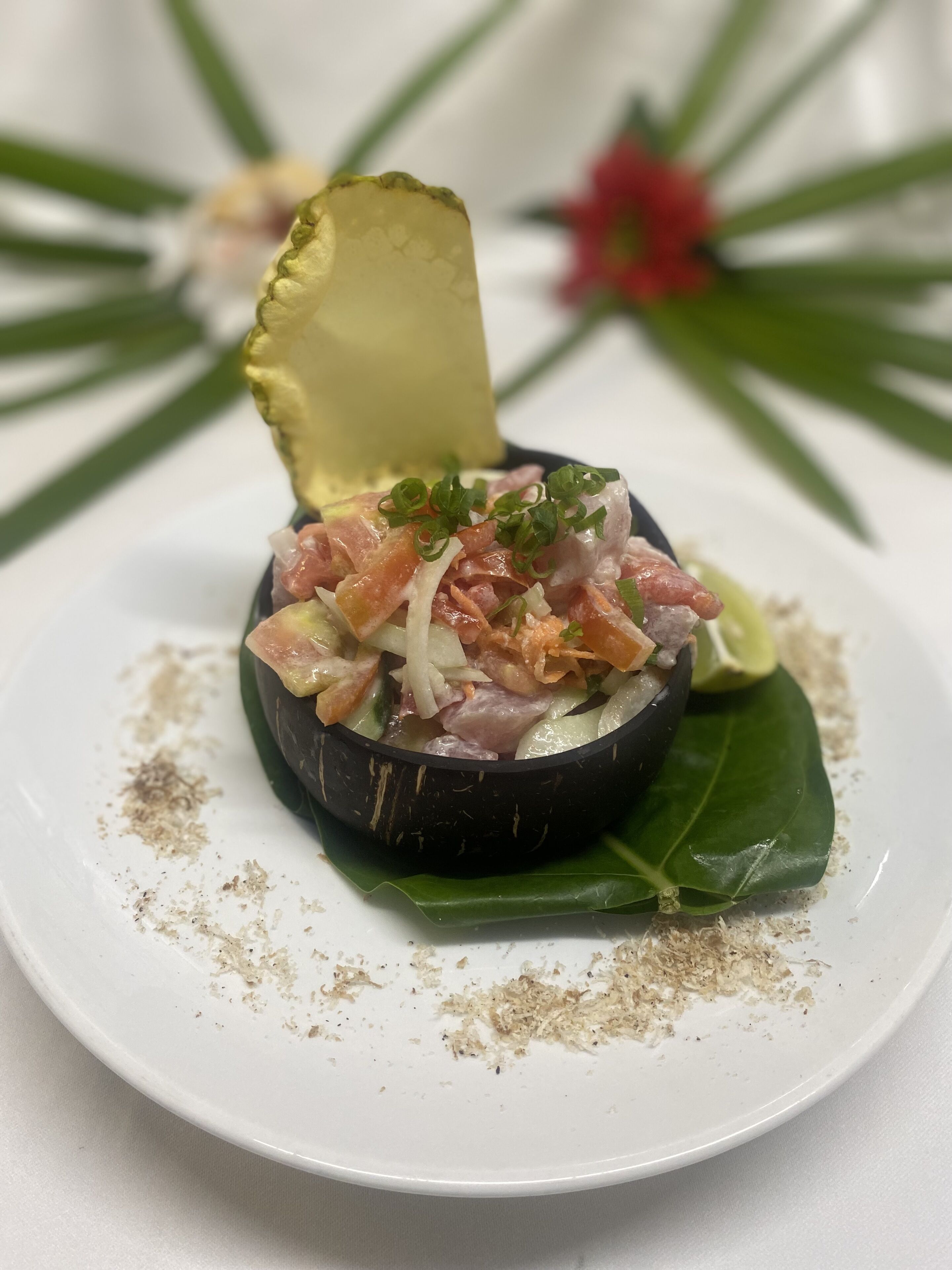 A dish with a black bowl on a white plate, garnished with green onions and surrounded by a green leaf.