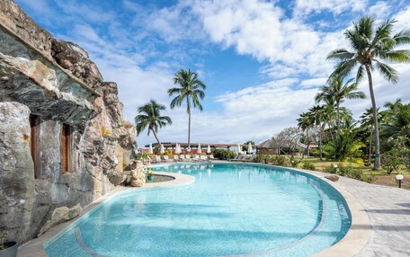 A swimming pool with a curved edge, surrounded by palm trees and a stone wall.