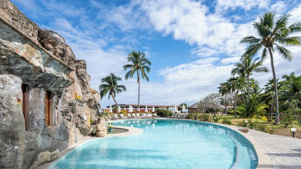 A swimming pool with a curved edge, surrounded by palm trees and a stone wall. - Hotel Royal Tahitien (Pirae)