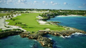 Campo de golf con vista al mar, que incluye una playa y afloramientos rocosos.