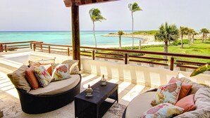 Un espacio de estar al aire libre cubierto con mobiliario de mimbre, una pequeña mesa y vistas a la playa y al océano.