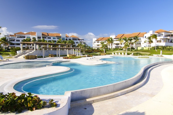 Un resort con una amplia piscina curvada rodeada de edificios blancos con techos rojos.