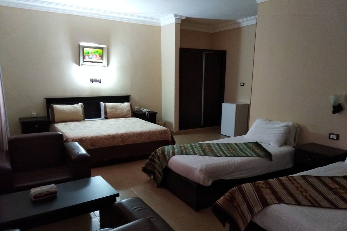 A hotel room with two beds, a sofa, a small table, a TV, and a wardrobe.