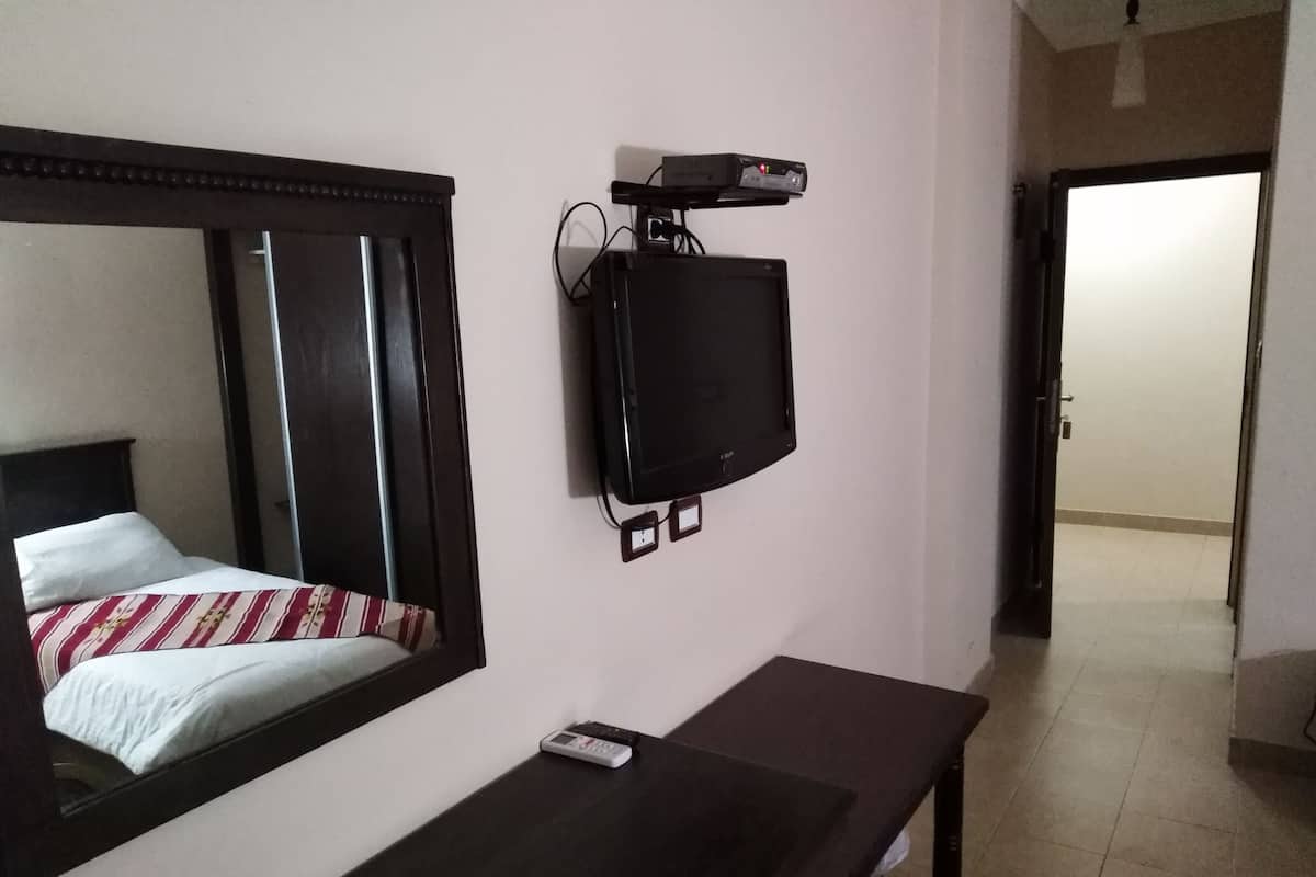 A hotel room with a bed, a TV mounted on the wall, a bedside table, and a door leading to another room.