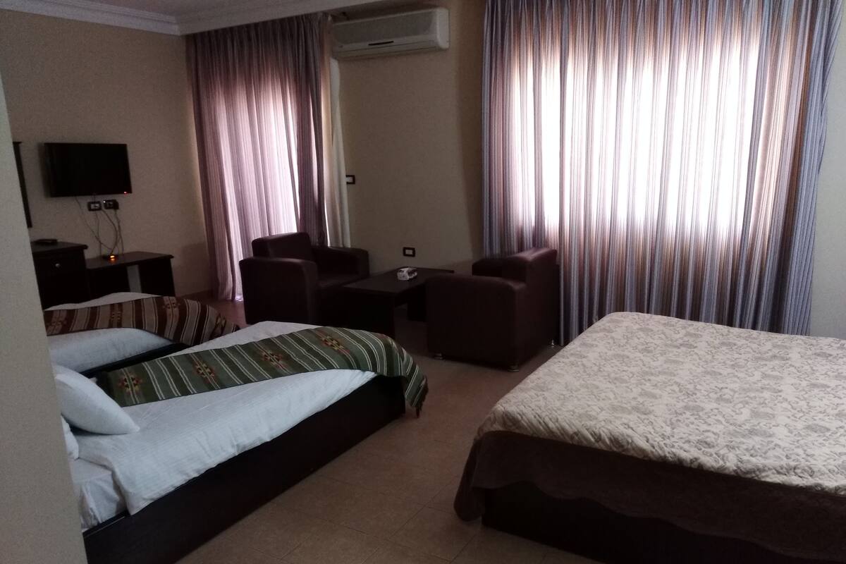 A hotel room with two beds, a desk, a chair, and a TV.