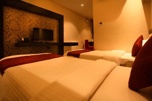 Une chambre d’hôtel avec deux lits, un téléviseur à écran plat fixé au mur et un fauteuil rouge.