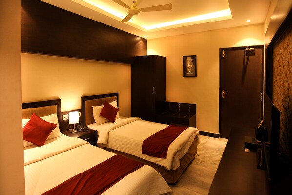 Une chambre d’hôtel avec deux lits, une armoire, un bureau avec une lampe et une porte.