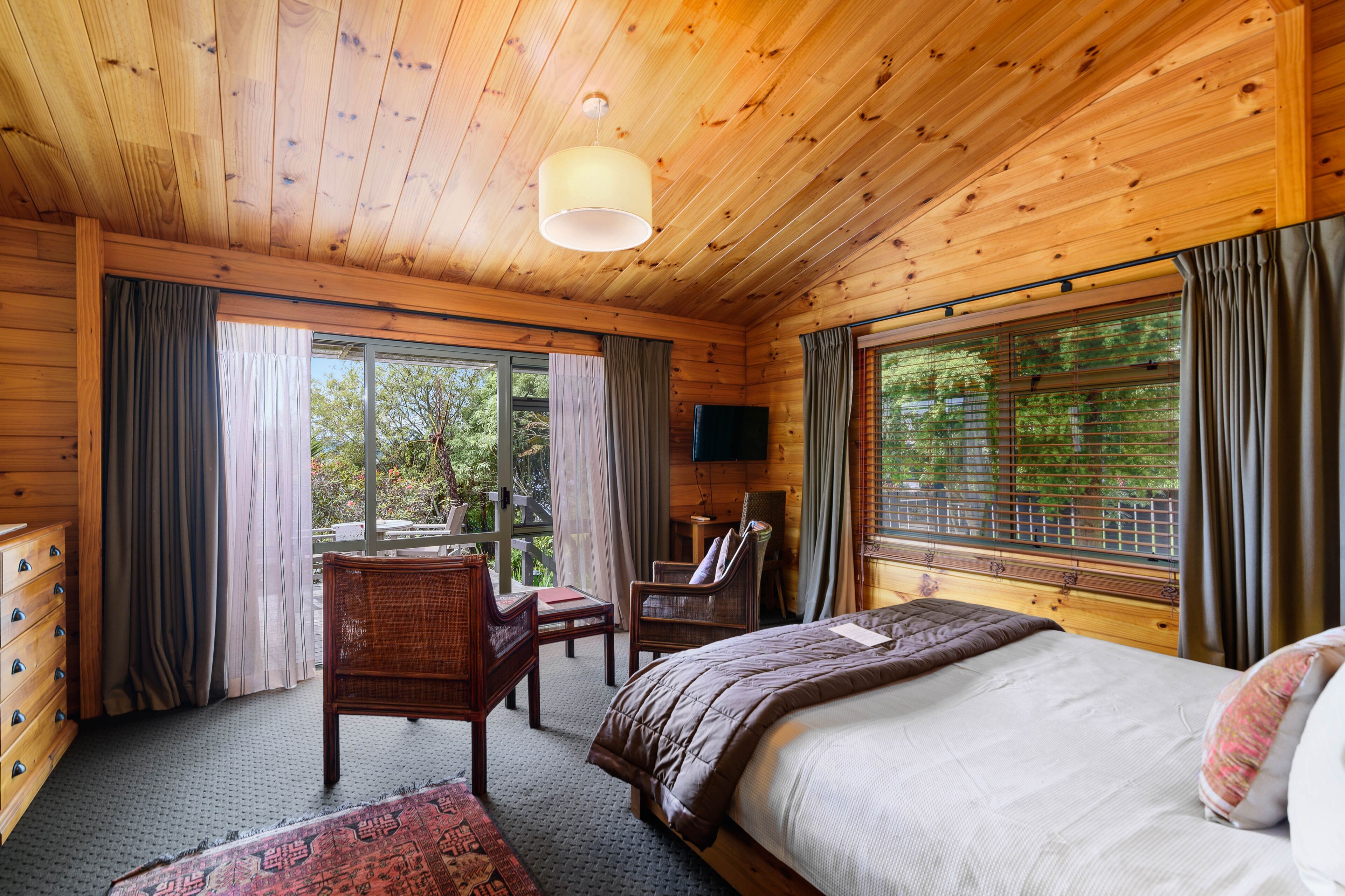 A wooden cabin bedroom with a bed, a chair, a desk, and a TV.