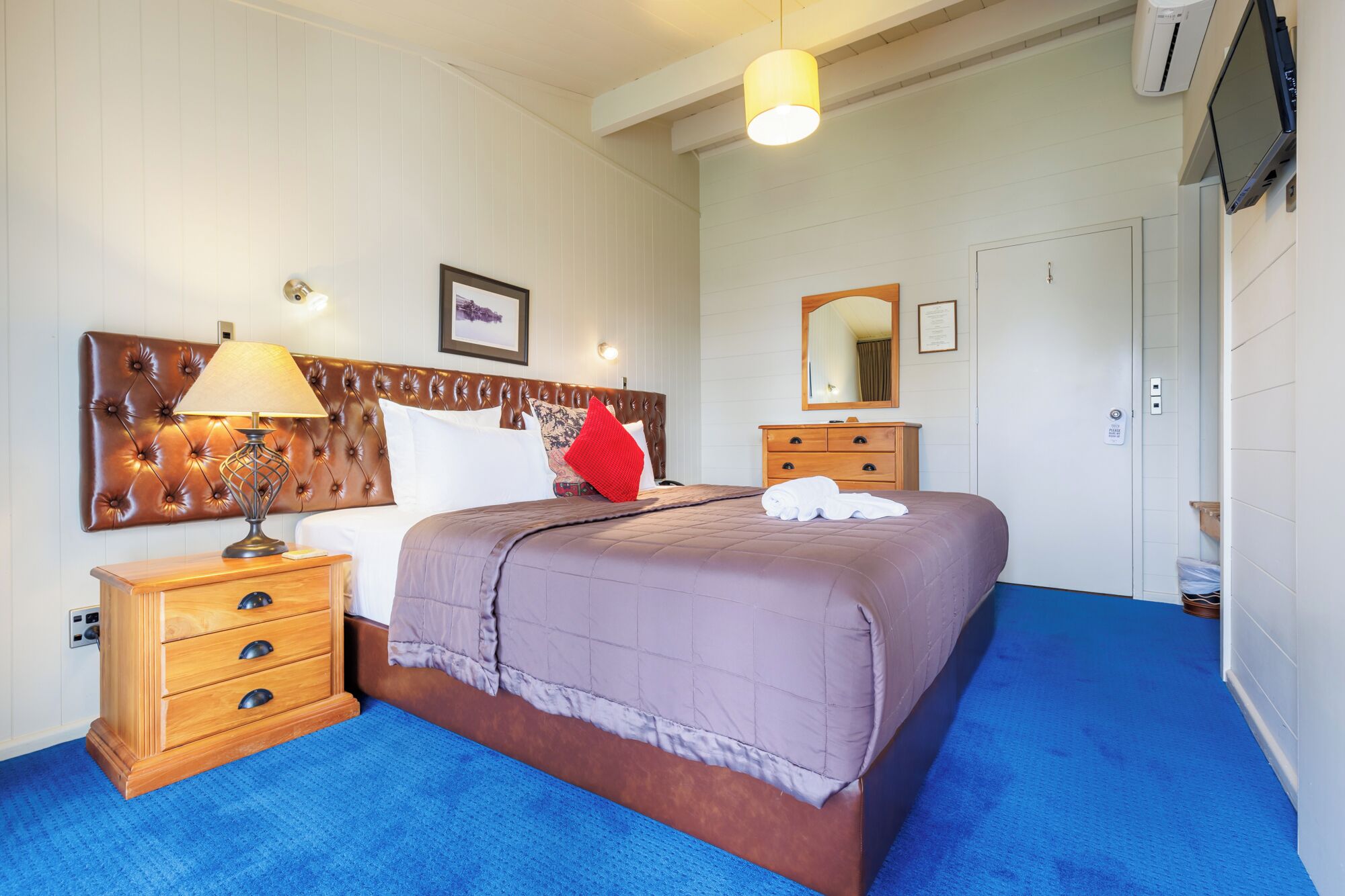 A hotel room with a large bed, a wooden nightstand, a dresser, and a television mounted on the wall.