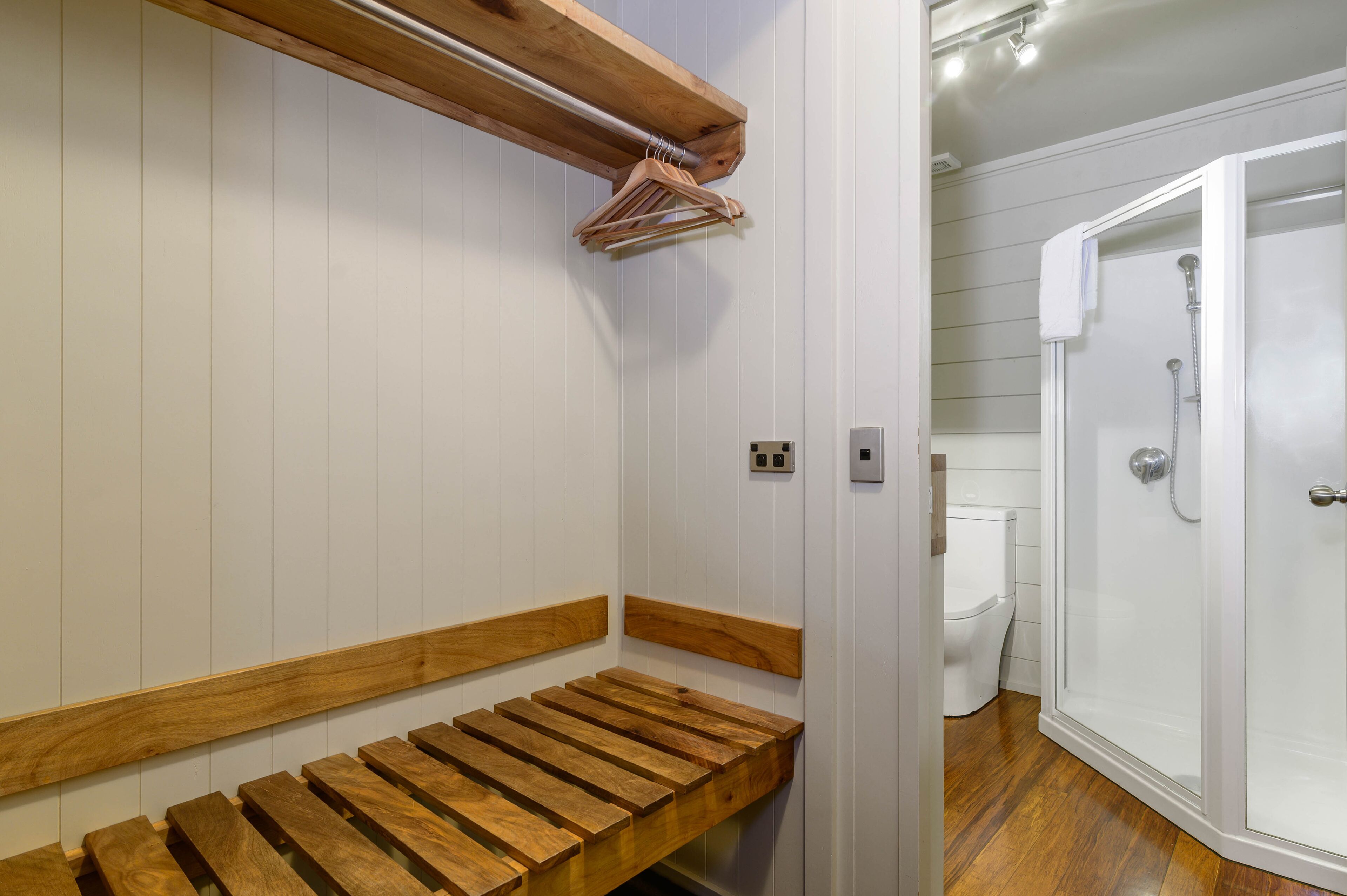 A bathroom with a wooden bench, a shower area, and a toilet.