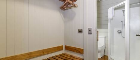 A bathroom with a wooden bench, a shower area, and a toilet.