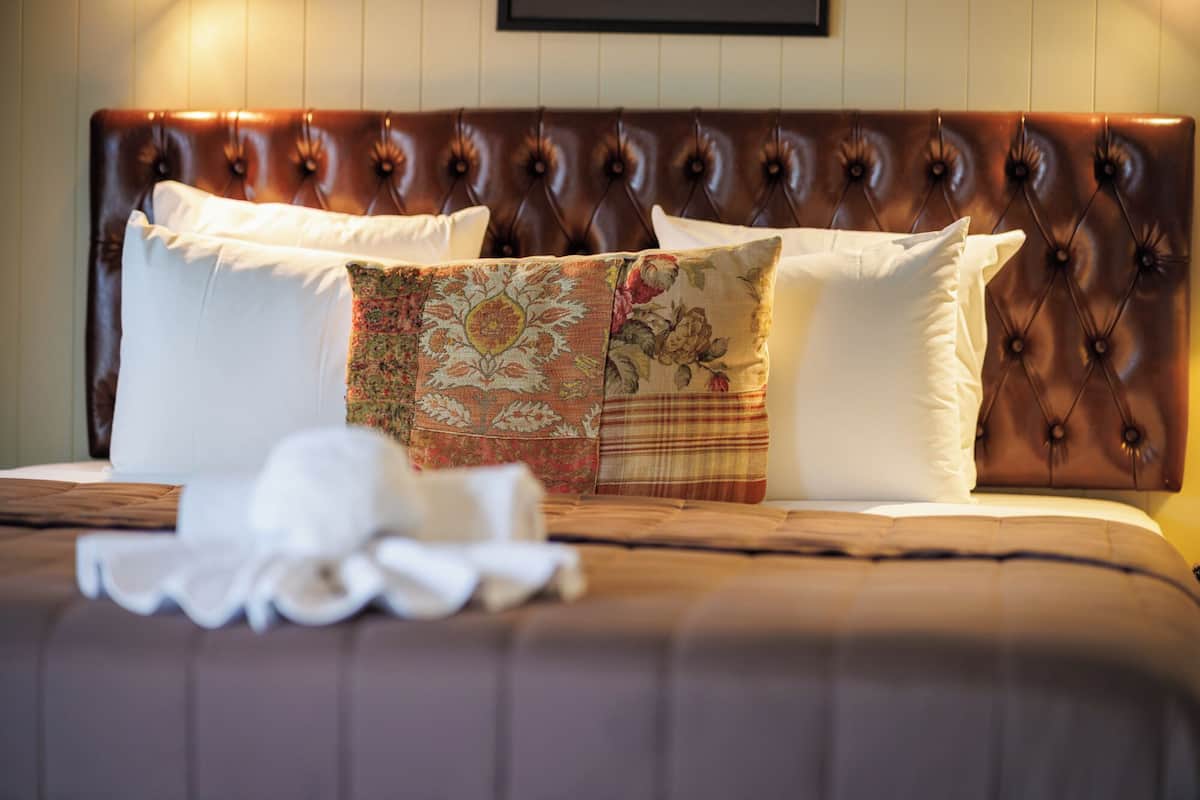 A bed with a brown headboard, white pillows, and a floral-patterned throw.