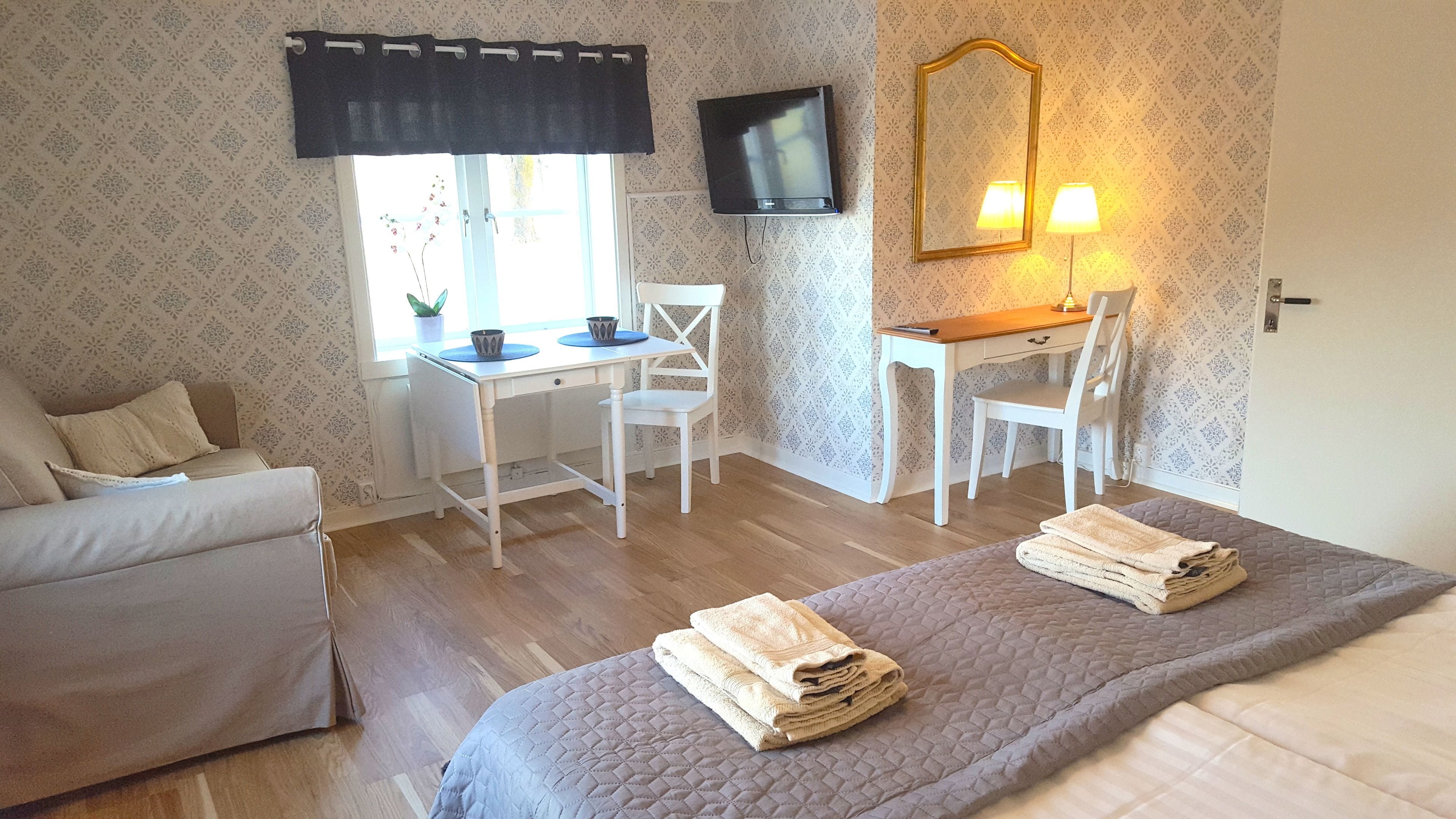 A hotel room with a bed, a desk, a chair, a TV, and a window with a curtain.