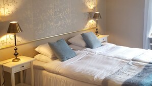Een slaapkamer met een groot bed, twee nachtkastjes met lampen, een decoratief paneel aan de muur en een witte vloerkleed.