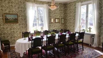 Comedor con una mesa redonda dispuesta para seis personas, sillas, papel tapiz con motivos florales y una araña.
