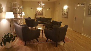 Een hotel lobby met een zithoek, inclusief banken en een salontafel, een kroonluchter en kunstwerken aan de wanden.