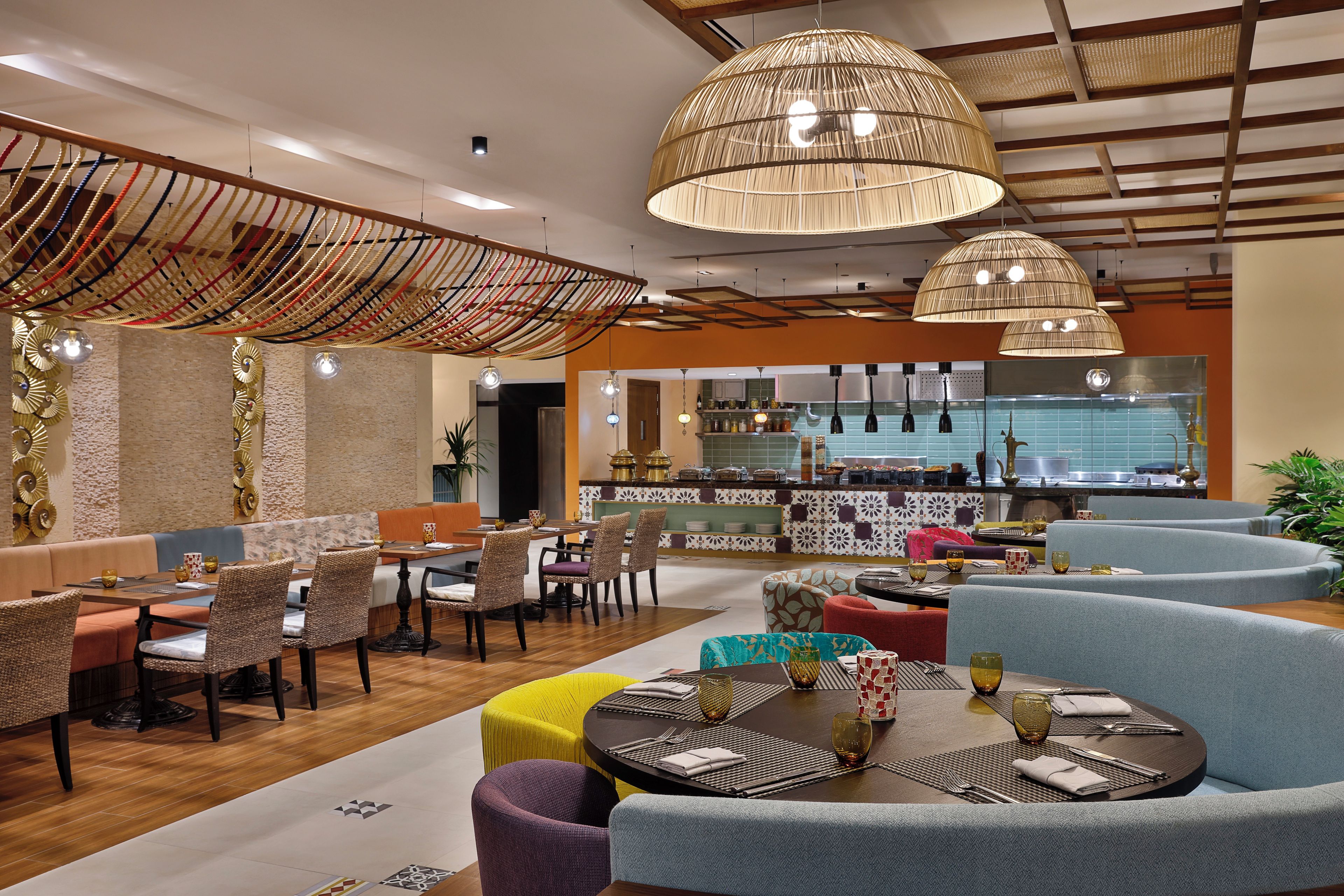 A modern dining area with round tables, wicker chairs, and a kitchen in the background.